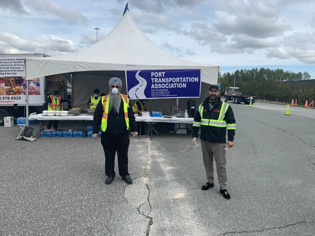 Two PTA volunteers in safety vests in front of the event tent at the Nordel scale, with catering tables behind them